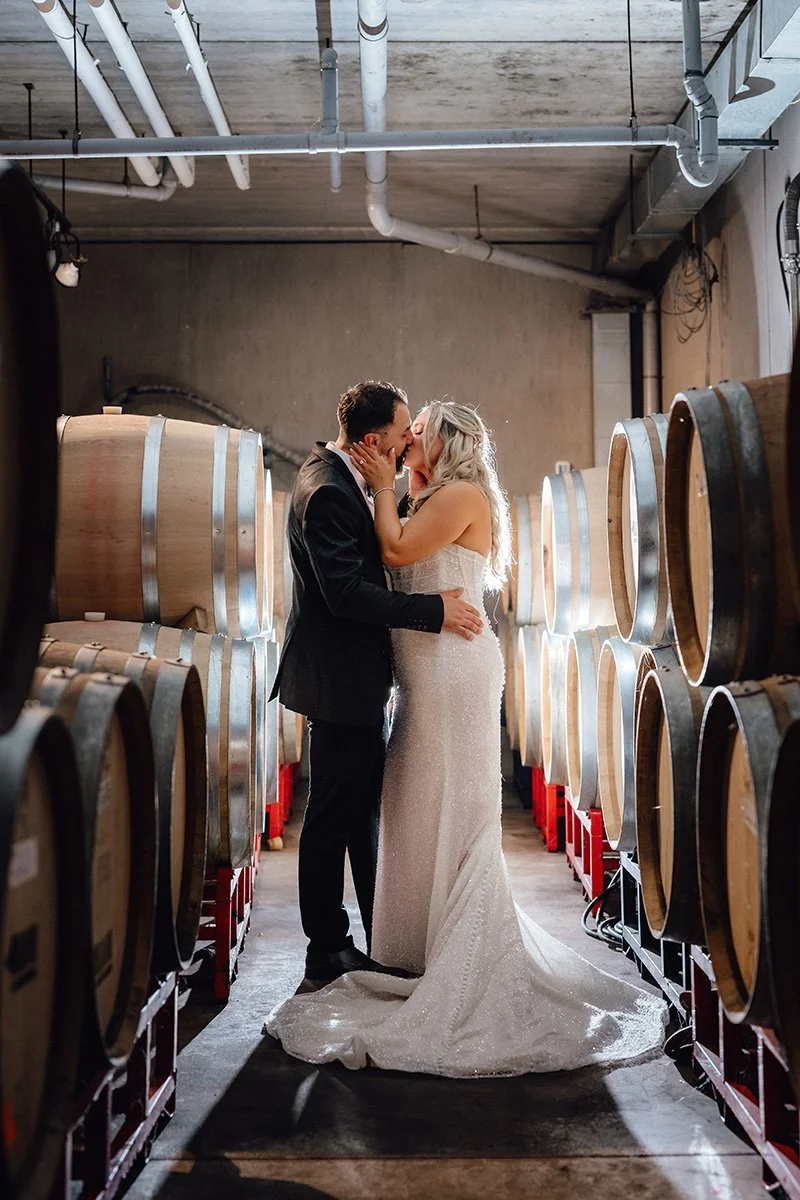backlit bride and groom embracing in the aisle of a winery barrel cellar