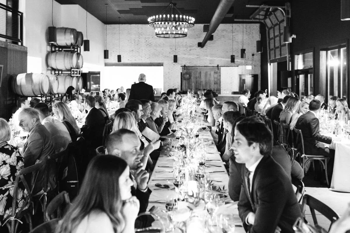view lengthwise down a long harvest table wedding reception setup while guests mingle by candlelight