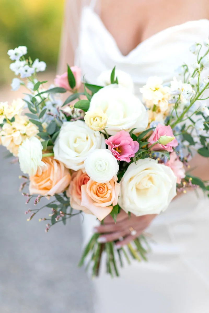 close view of a bridal bouquet with white and peach roses, white ranunculus, light blue stock, and pink lisianthus flowers