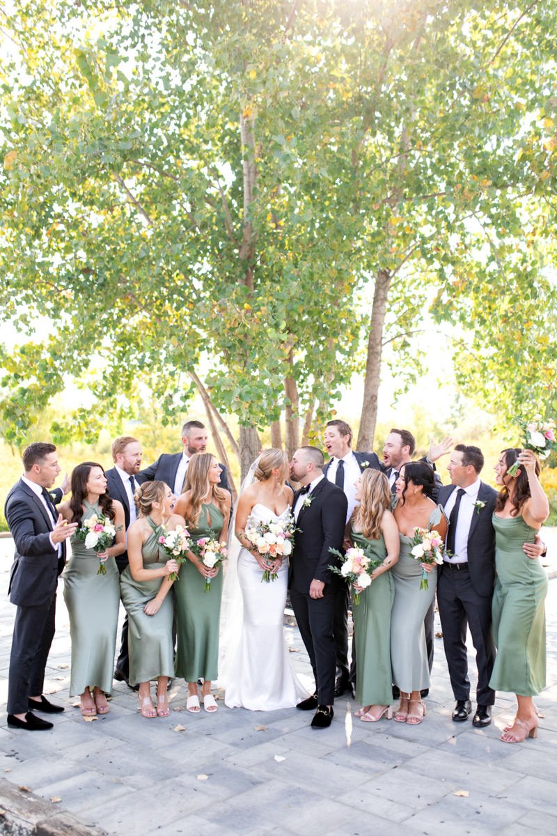 bride and groom kiss while their bridesmaids and groomsmen cheer around them