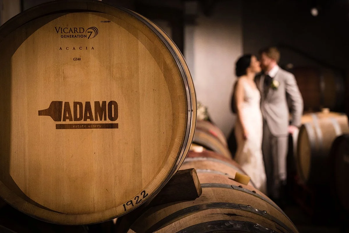 adamo estate winery wine barrel with bride and groom in the background out of focus in the barrel cellar