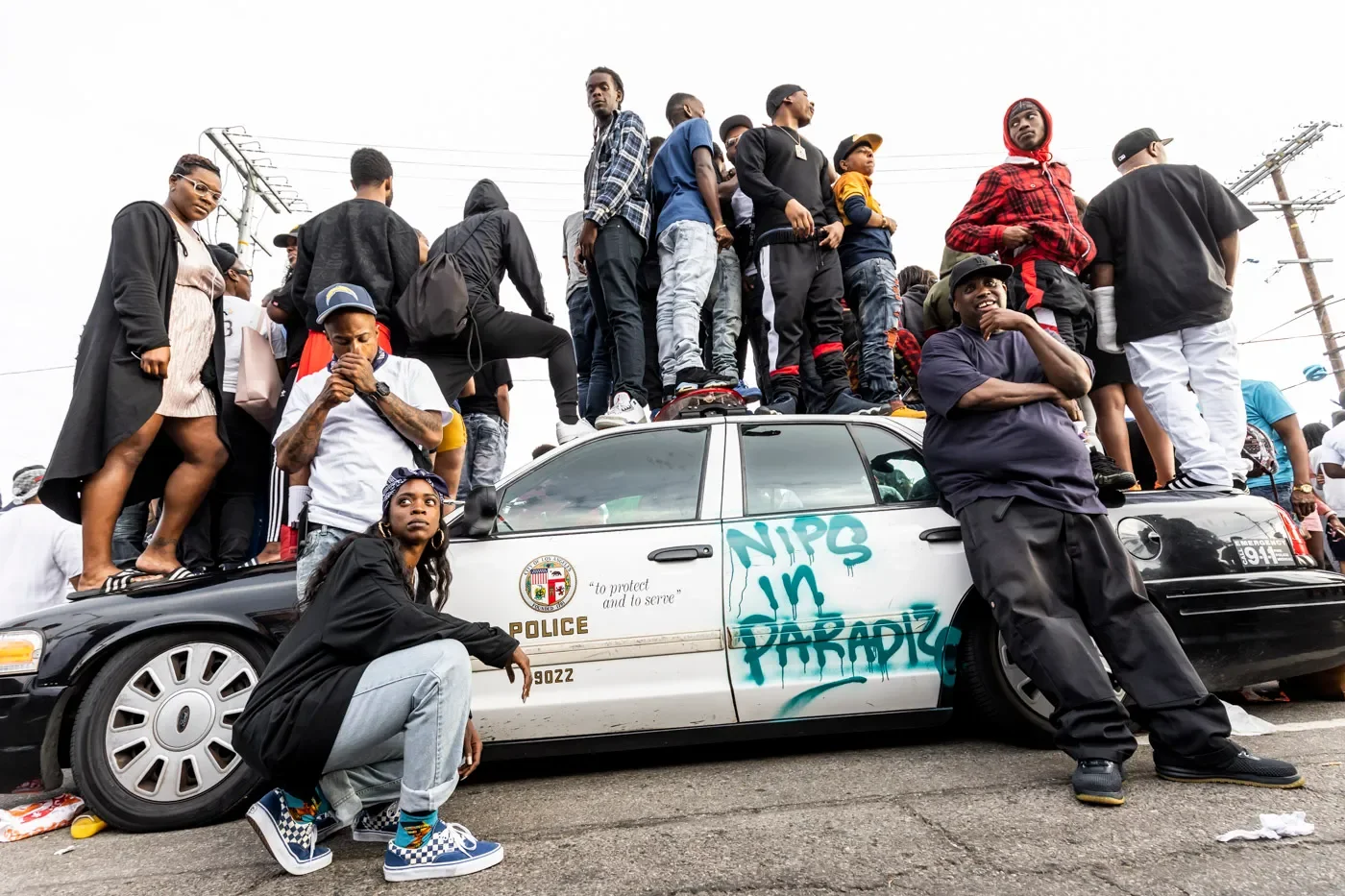 Community observes the funeral procession for Nipsey Hussle on top of a Los Angeles police car on Slauson and Crenshaw Avenue on April 11, 2019.
