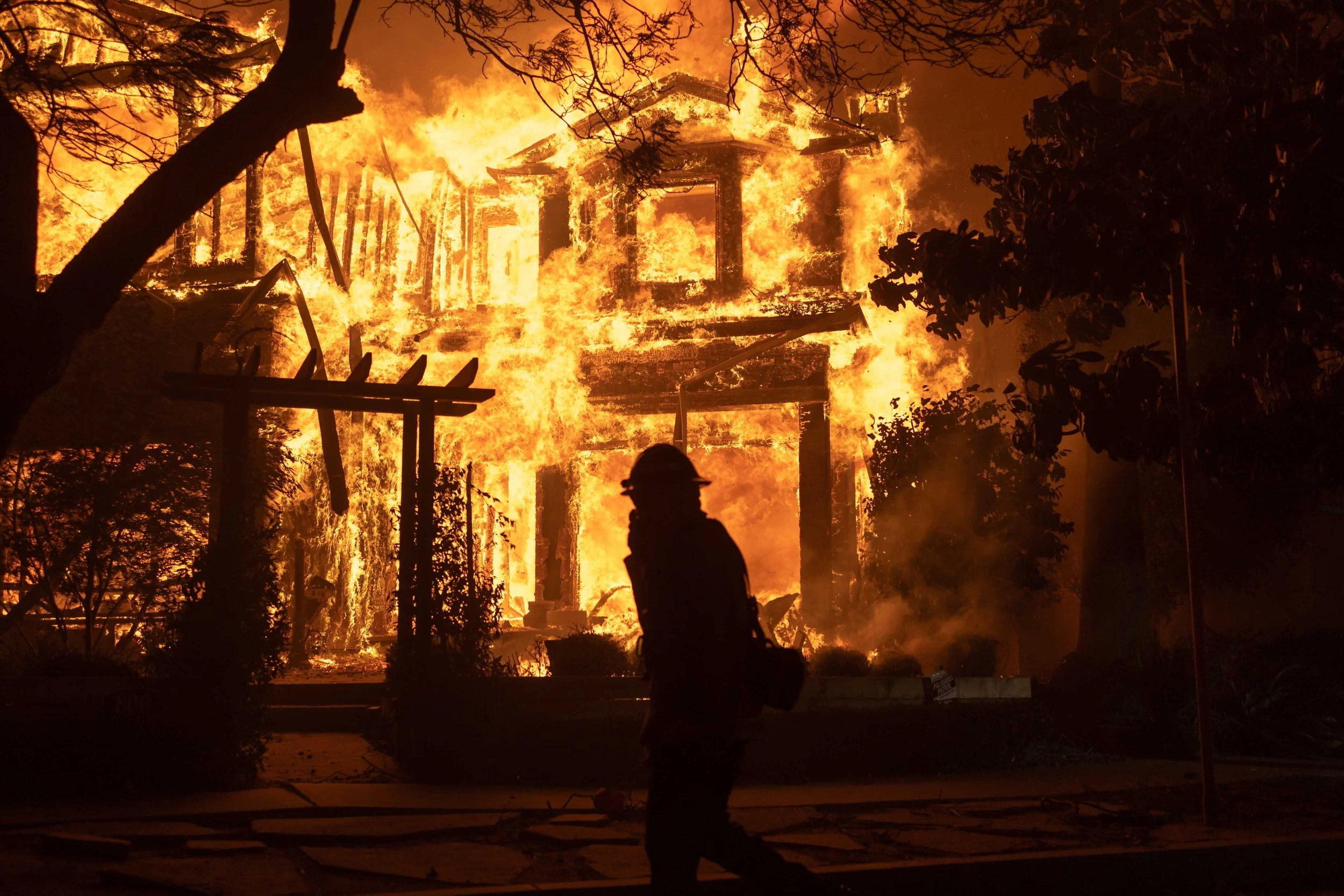 A firefighter walks past a burning home in the Palisades fire on January 7, 2025.