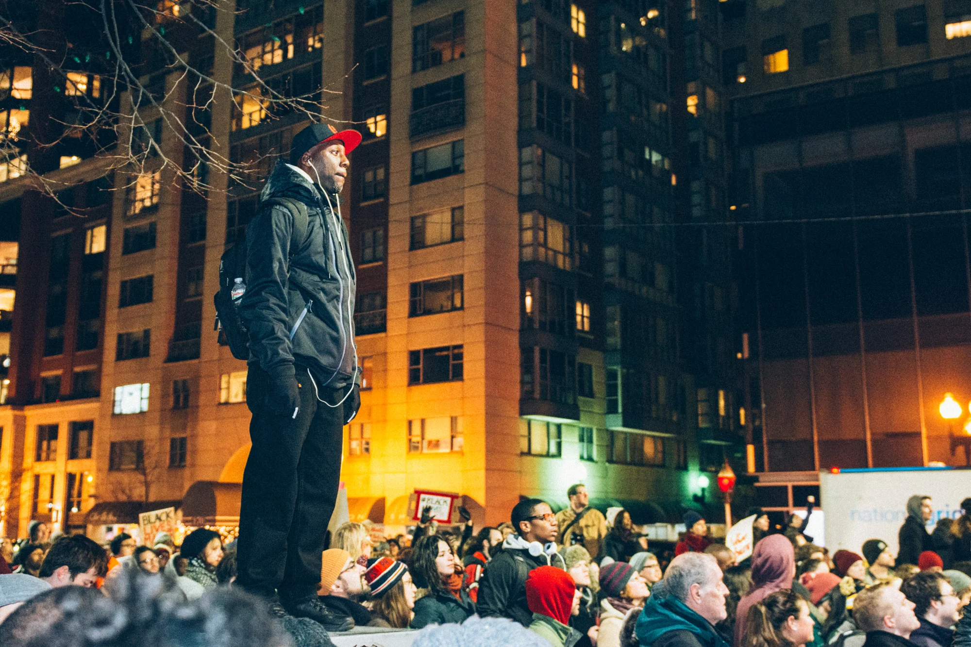 Man standing on an electrical transformer to get a better view of the speakers in the crowd.