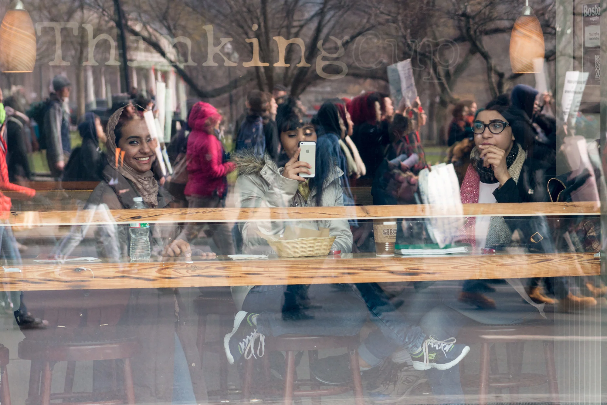 Three women in a coffee shop looking out and taking pictures of the march