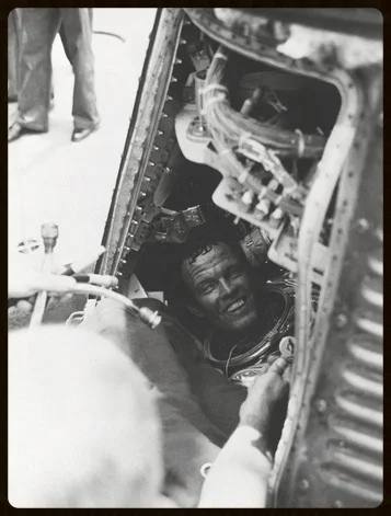 Gordon Cooper as first seen when his Mercury Atlas-9 capsule hatch is opened aboard the recovery ship after his flight. Tucked safely in one of his suit pockets, the flown $2 bill.