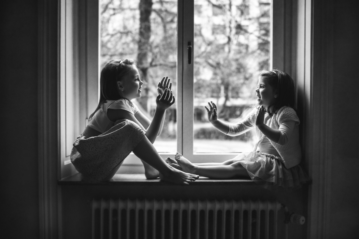 Black-and-white-image-of-sisters-playing-in-window-by-Stockholm-barnfotograf-Sandra-Jolly.jpg