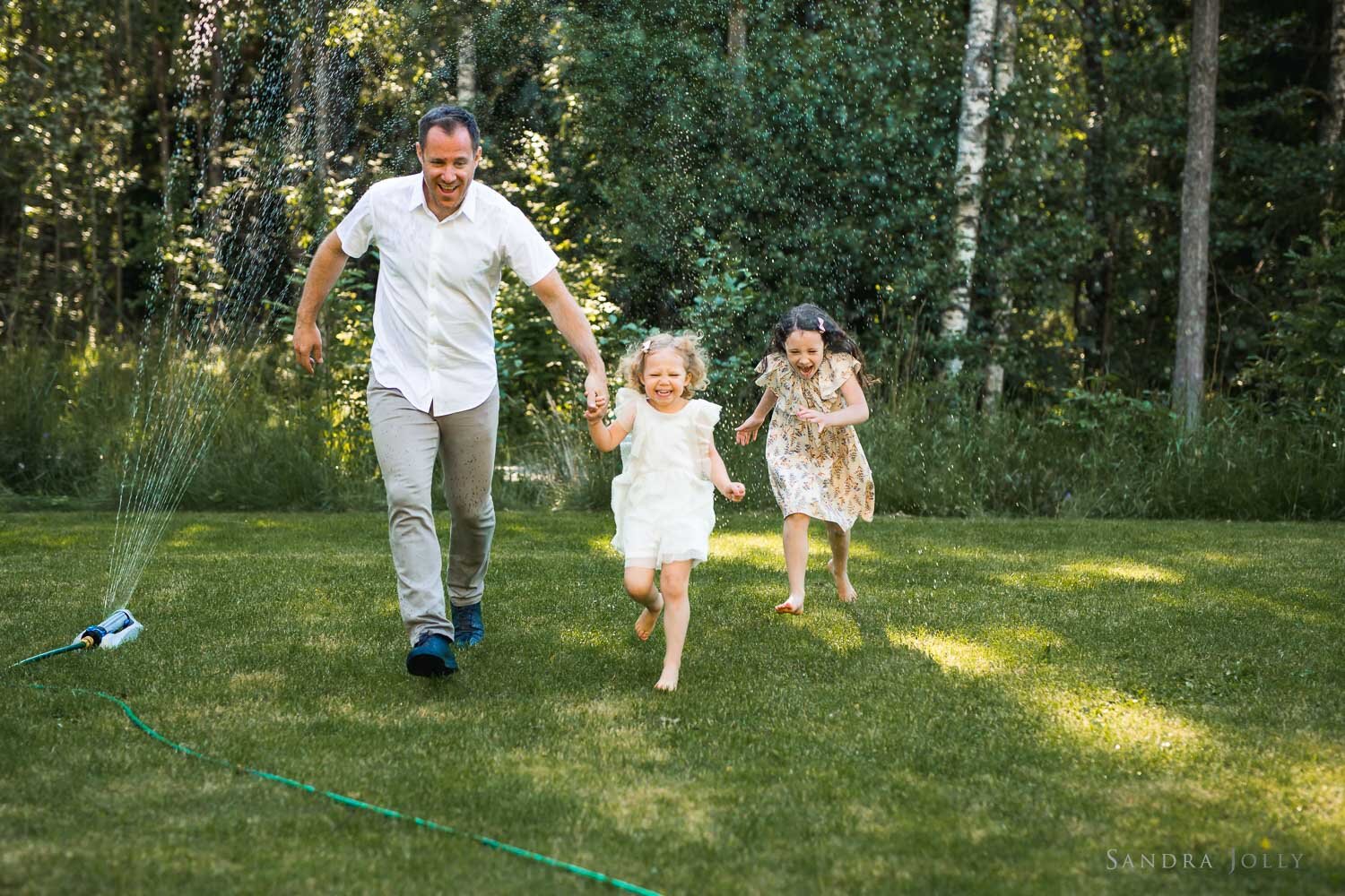dad-and-daughters-running-through-sprinkler-by-sandra-jolly-photography.jpg