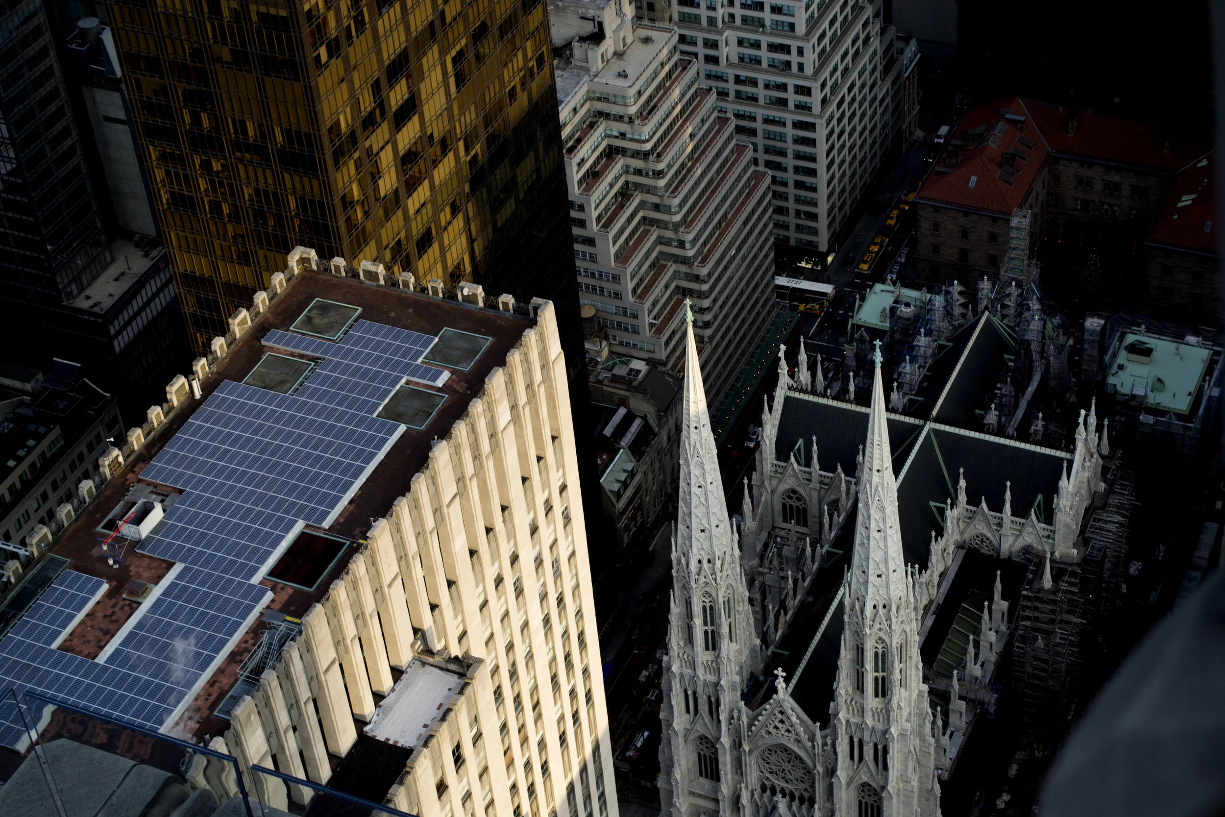 View of tall city buildings from a high vantage point, including a Gothic-style church with pointed spires and a rooftop with solar panels.