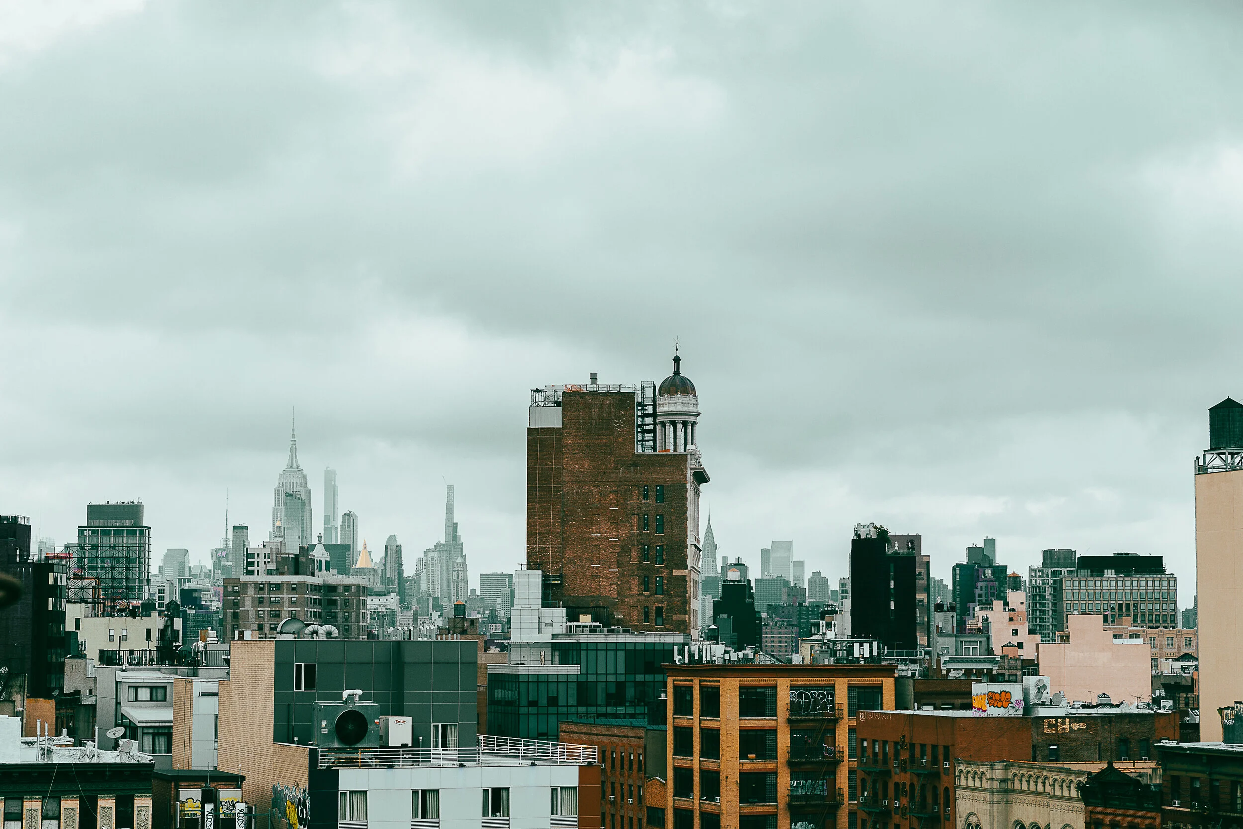 Cityscape of New York City with numerous tall buildings and clouds overhead.
