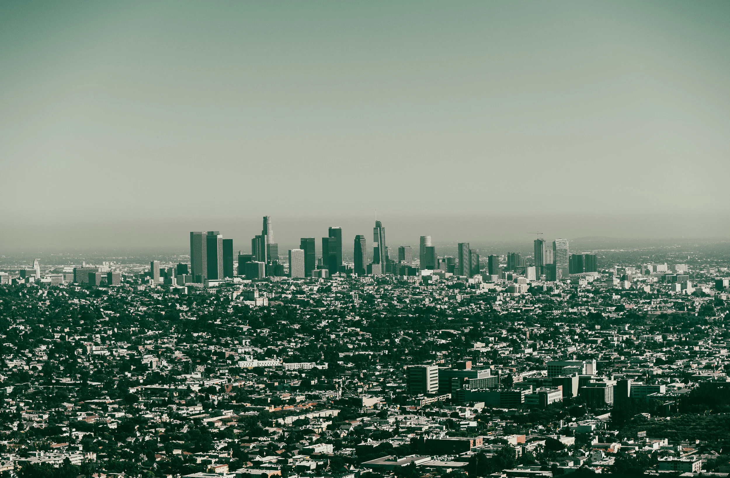City skyline with tall skyscrapers in downtown Los Angeles, viewed from a distance, with a clear sky overhead.