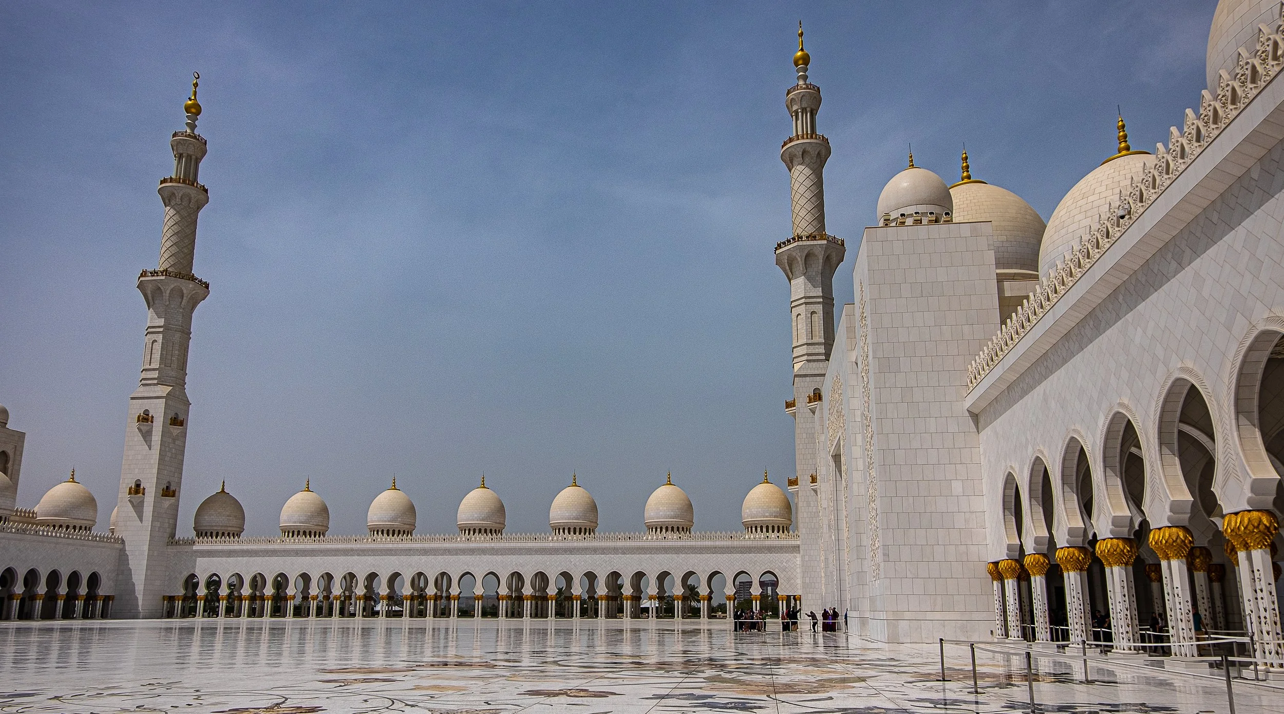 White mosque in Abu Dhabi, UAE with multiple minarets and domes under a clear blue sky.