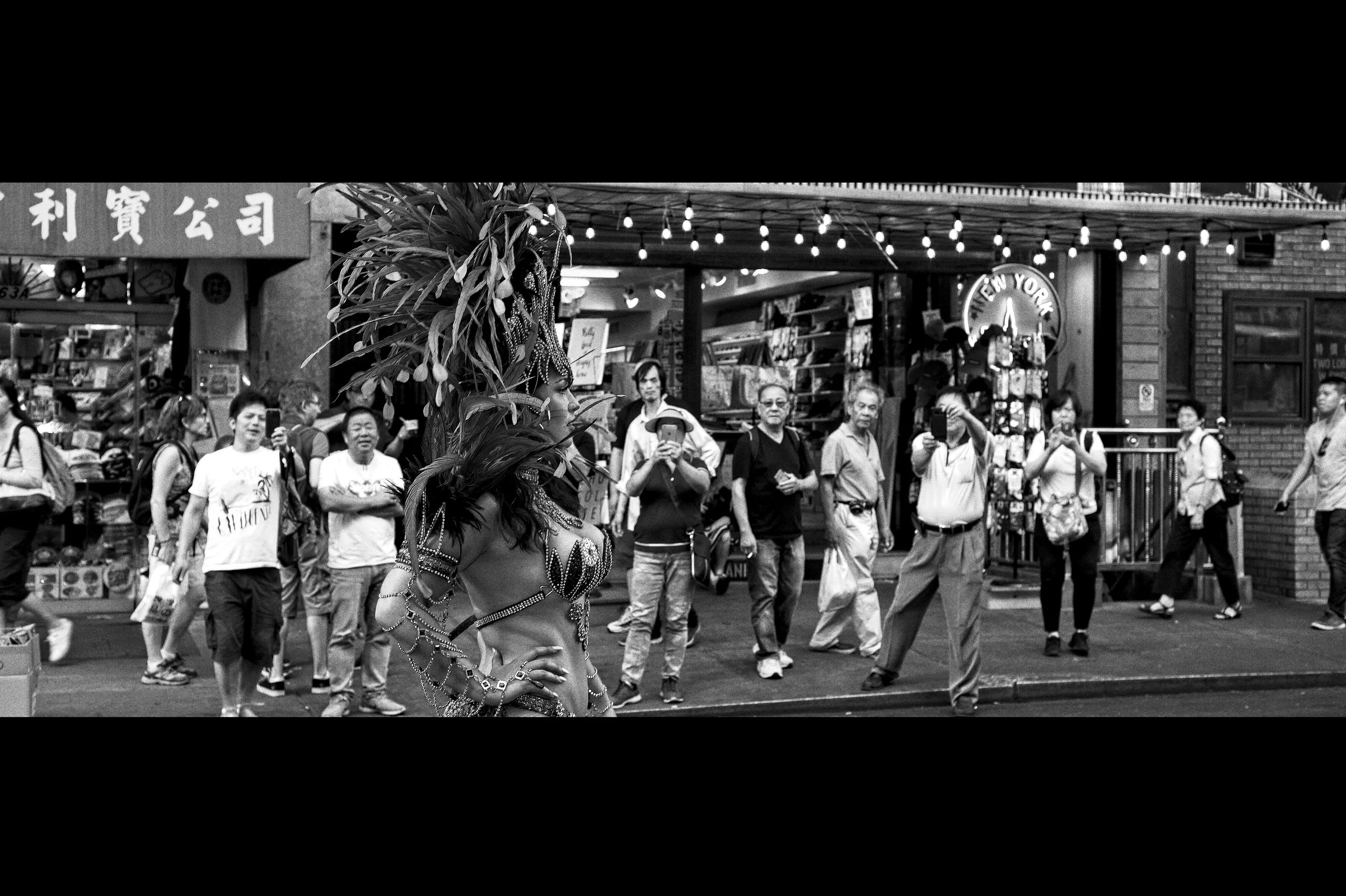 Cinematic black and white street portrait of Karolina Finskas in an elaborate Carnival feather headpiece walking through Chinatown, NYC.