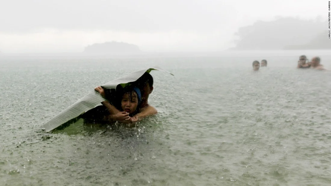10. A man and girl use a banana leaf to cover themselves from the rain as they in the sea on the outskirts of Colon, Panama.