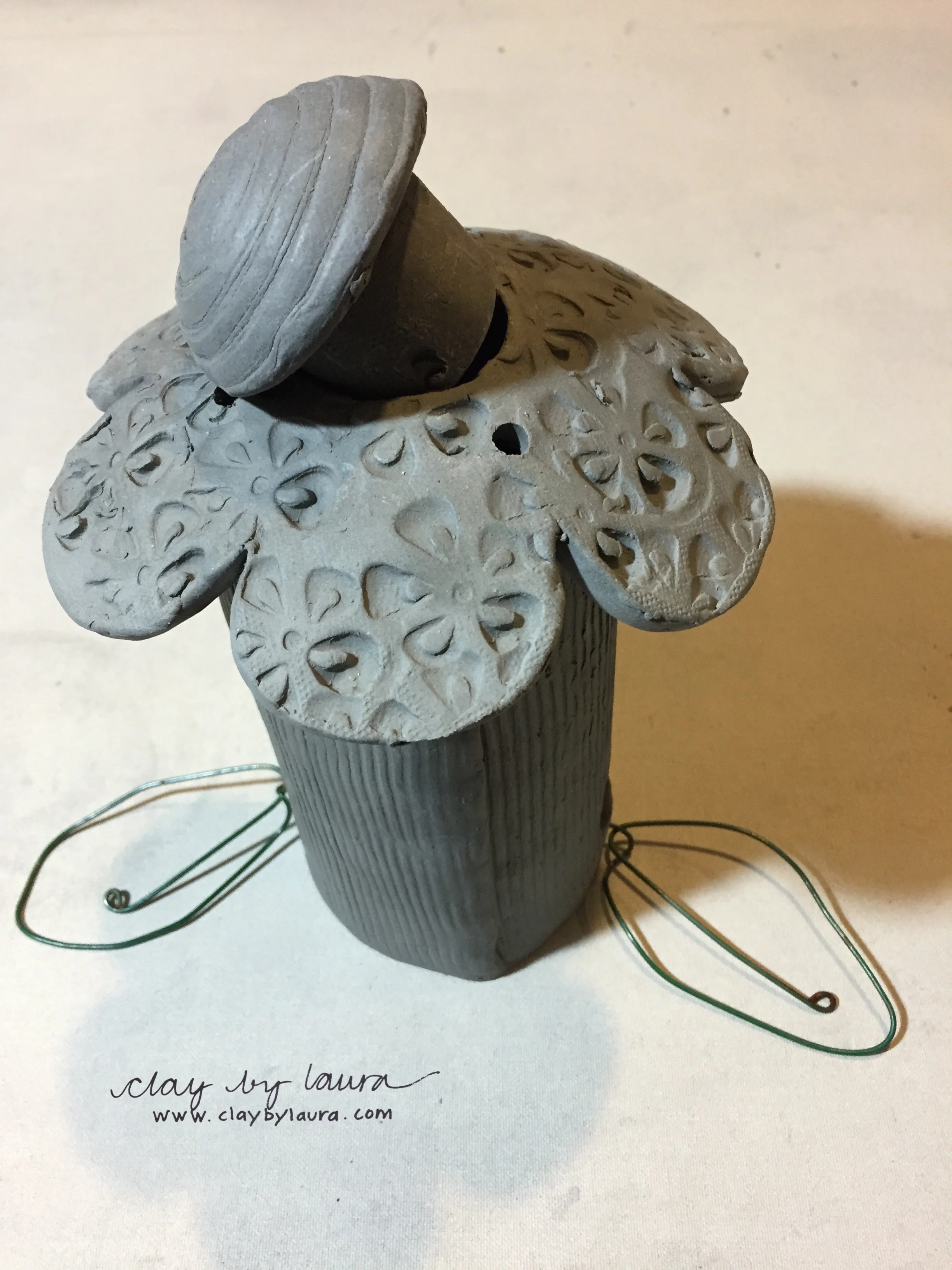 Here you can see where I made improvements to the functionality of the bird feeder. I kept the same flower shape for the top of the feeder. I made the center of the flower removable so bird seed can easily be added to the feeder. I will still use buttons and fishing line as I did in the original design to suspend the flower once it has been glazed and fired. I changed the design of the feeding perch. I decided to use wire bent to look like flower leaves instead of the clay ones I created in the original design. I'll add these at the same time as the buttons and fishing line. I'm happy with these improvements and I think this bird feeder has been 'changed for the better!" 
