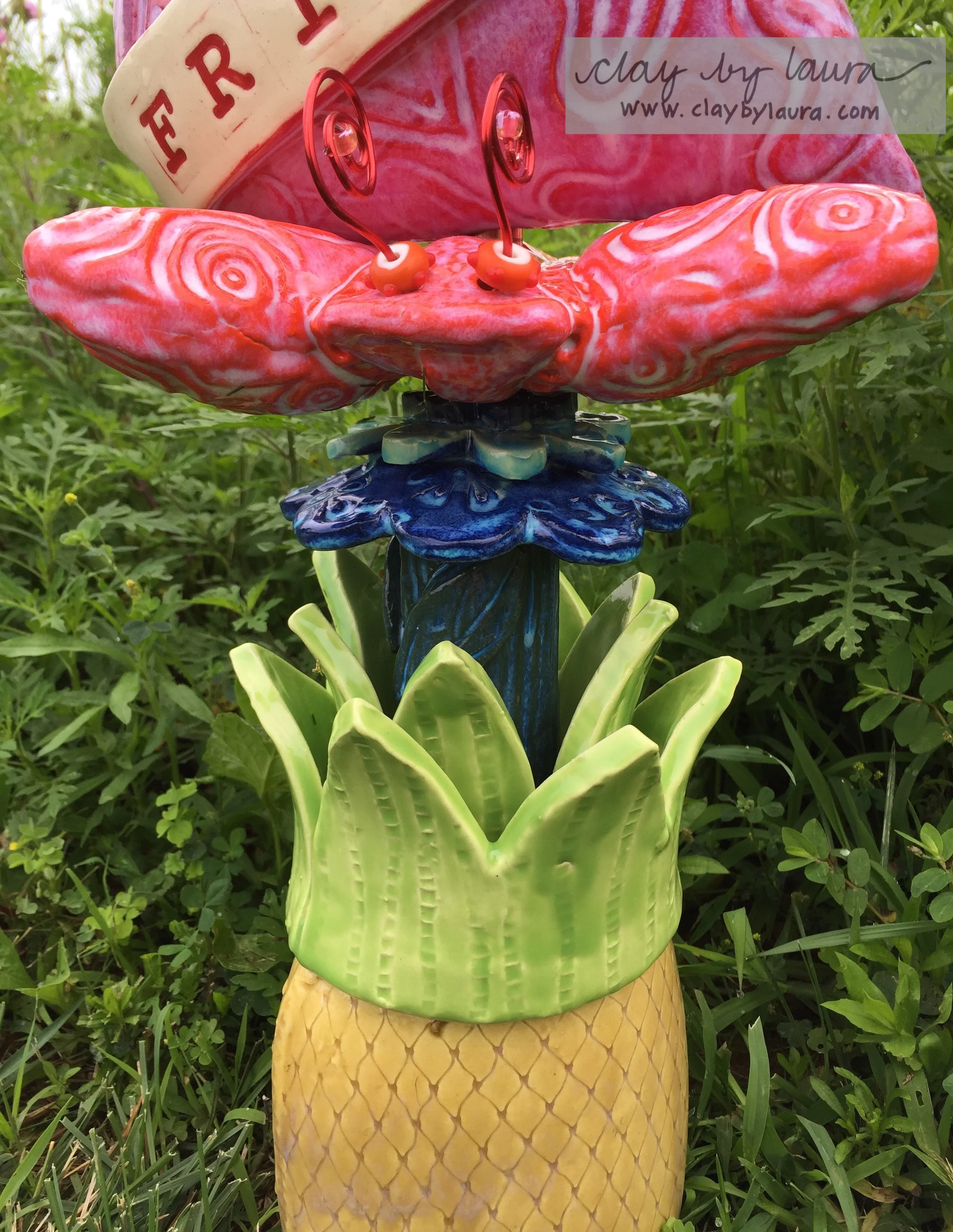 The base of this totem is a pineapple which has long been a symbol of welcome. The texture was created with the plastic webbing you often find securing fruits and vegetables in the produce department at the grocery store. I have a large 'cache' of texture-making materials around the studio just waiting for the right project! The butterfly resting atop an ocean-blue flower is representative of the Monarch Butterfly often seen throughout this southern isle. I use colorful wire and glass beads to complete this shape. 