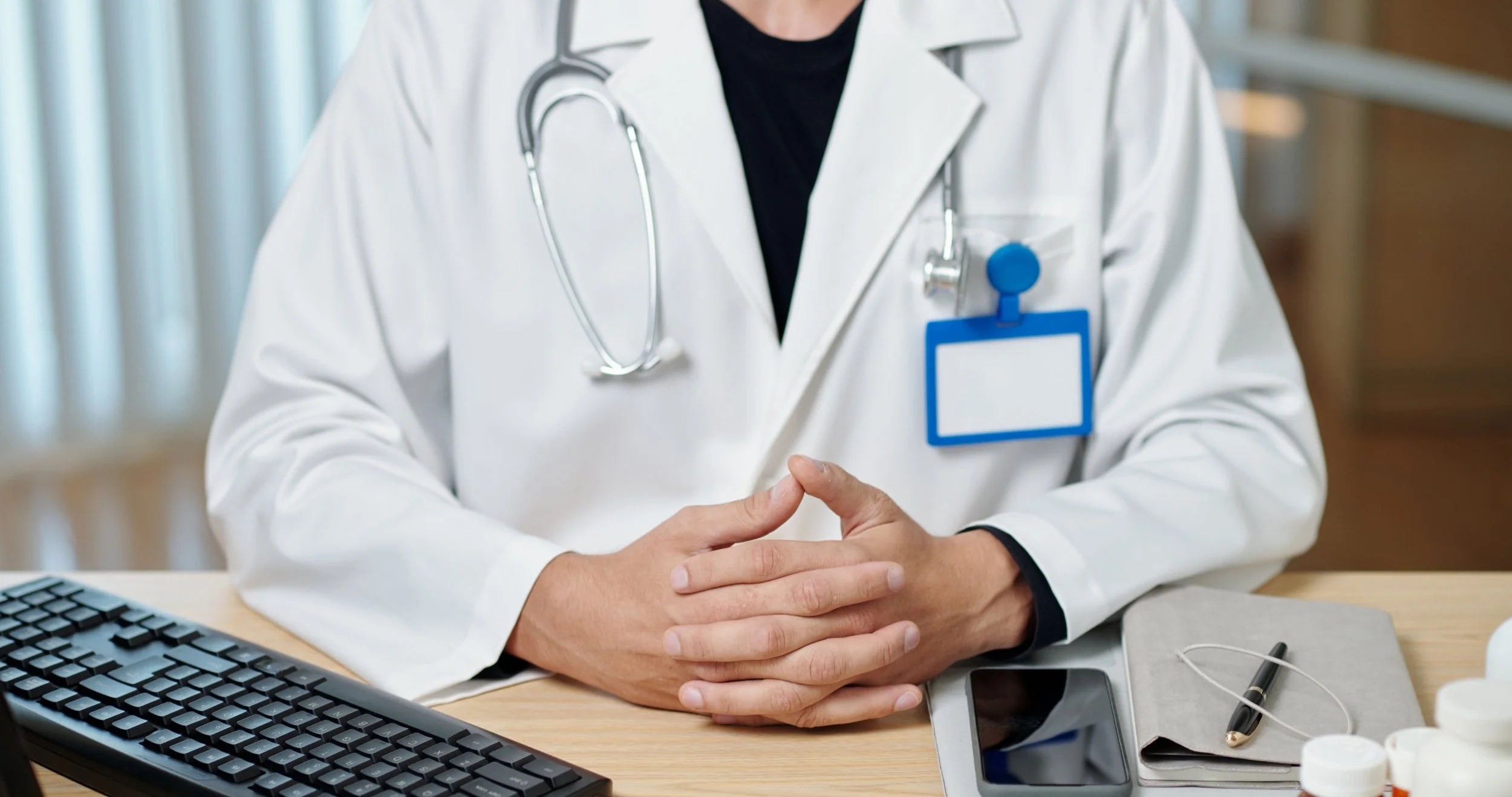 Interim CEO Search - image of doctor sitting at desk with hands folded and keyboard and phone on desk