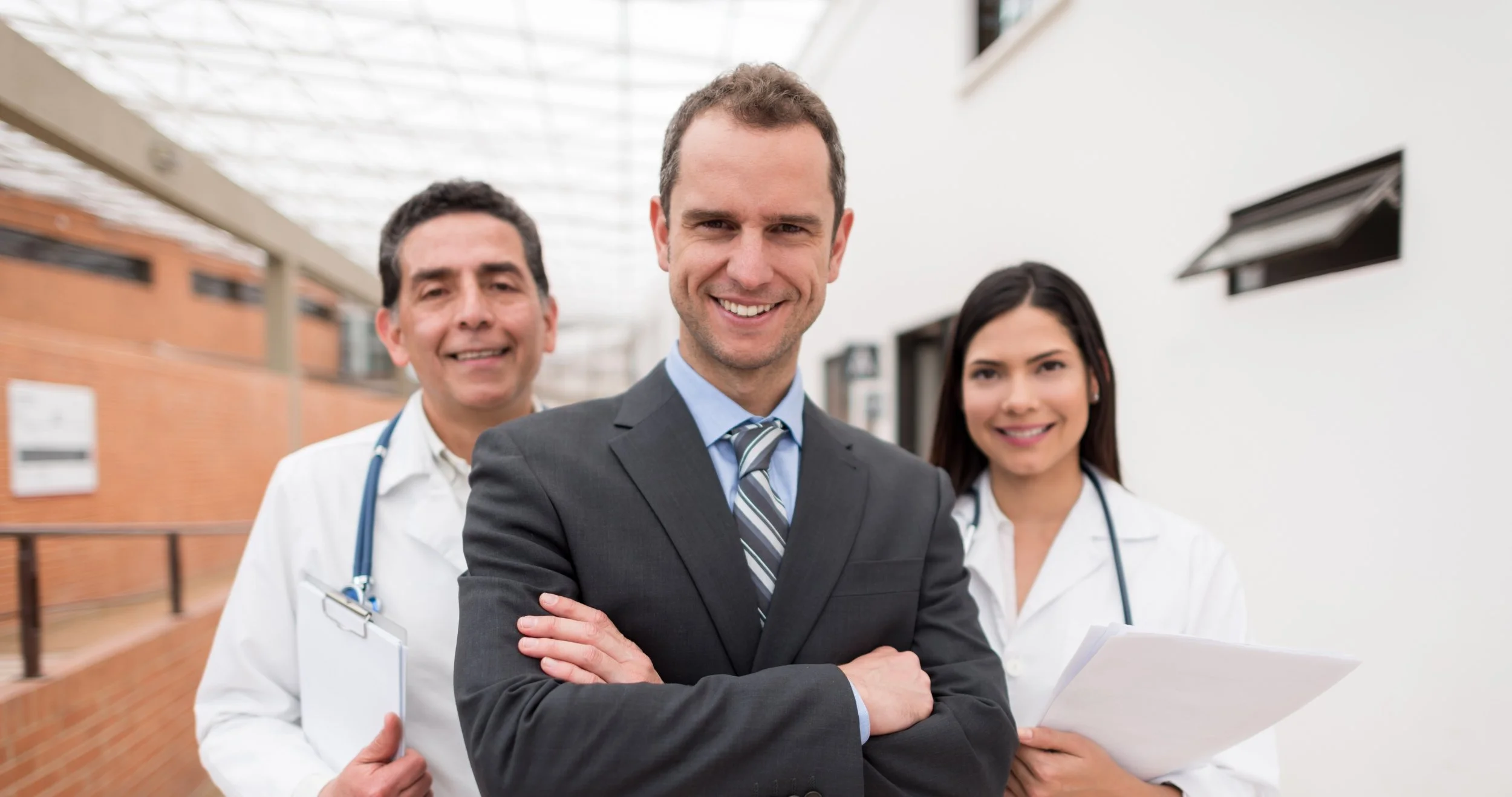 Interim Healthcare CEO Search - image of male interim healthcare CEO standing in front of male doctor and female doctor with arms crossed