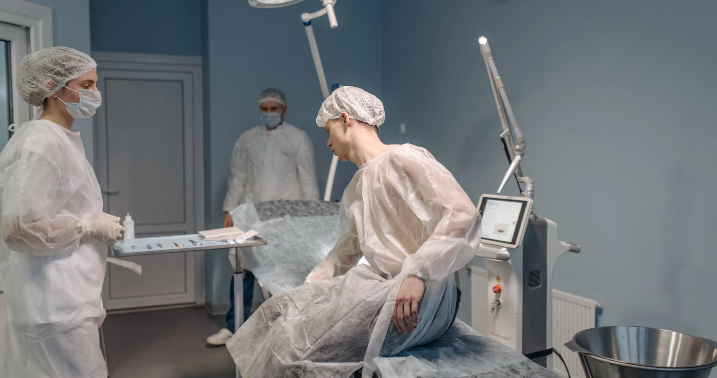 Interim Perioperative Director Search - image of patient getting ready to lay down on table in operating room with nurses around him prepping for surgery