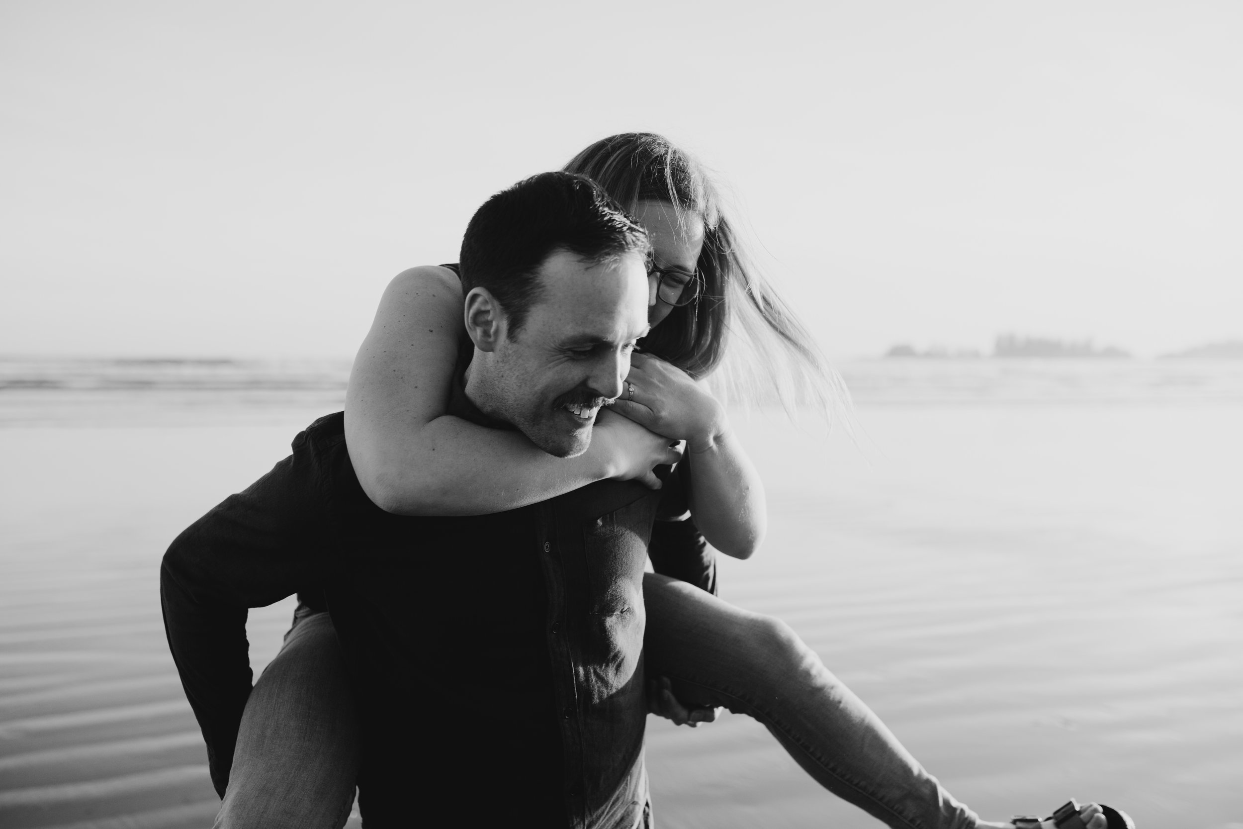 Girl getting a piggy-back from her fiancé, on Long Beach, Tofino, Vancouver Island, black and white image