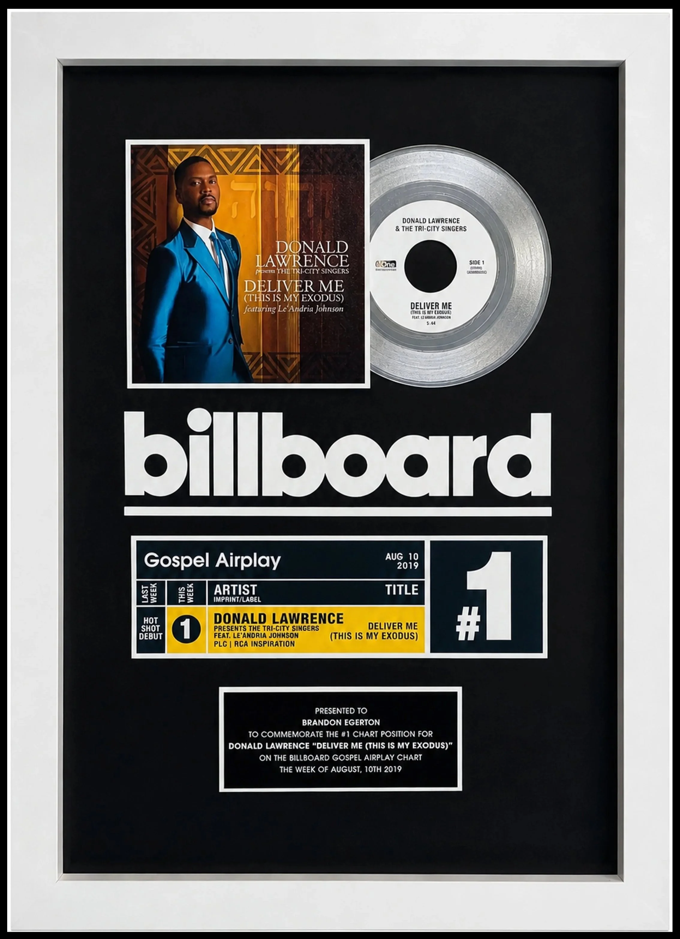 A framed Billboard chart award for gospel singer Donald Lawrence, featuring his song 'Deliver Me (This Is My Exodus)' featuring Le’Andria Johnson. The award includes a silver vinyl record and a photo of Donald Lawrence. Presented to Brandon Egerton.