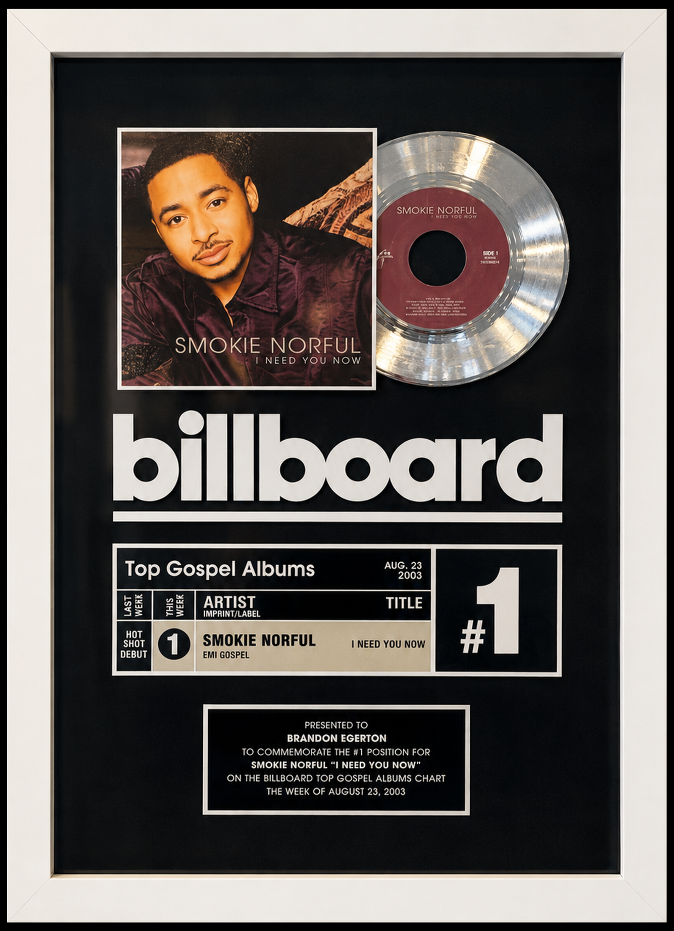 A framed music award plaque featuring a gold record and a photo of Smokie Norful on a Billboard top gospel albums chart commemorating his number one debut album 'I Need You Now' for the week of August 23, 2003. Presented to Brandon Egerton.