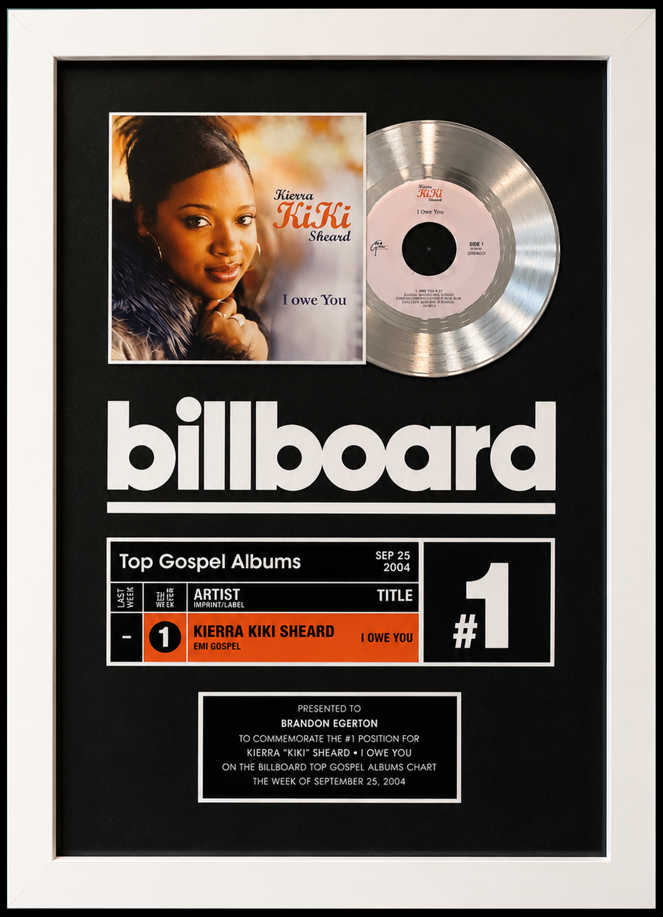 A framed Billboard chart plaque celebrating Kierra 'Kiki' Sheard's No. 1 gospel song 'I Owe You' from the album in September 2004. The plaque features a photo of Kierra Sheard, a silver record and chart information. Presented to Brandon Egerton.