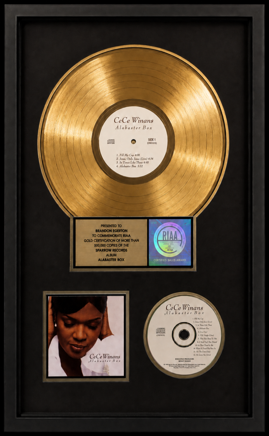 A framed platinum record award for CeCe Winans' album "Alabaster Box," featuring a gold record, a photograph of CeCe Winans, and a record label with song titles. Presented to Brandon Egerton.