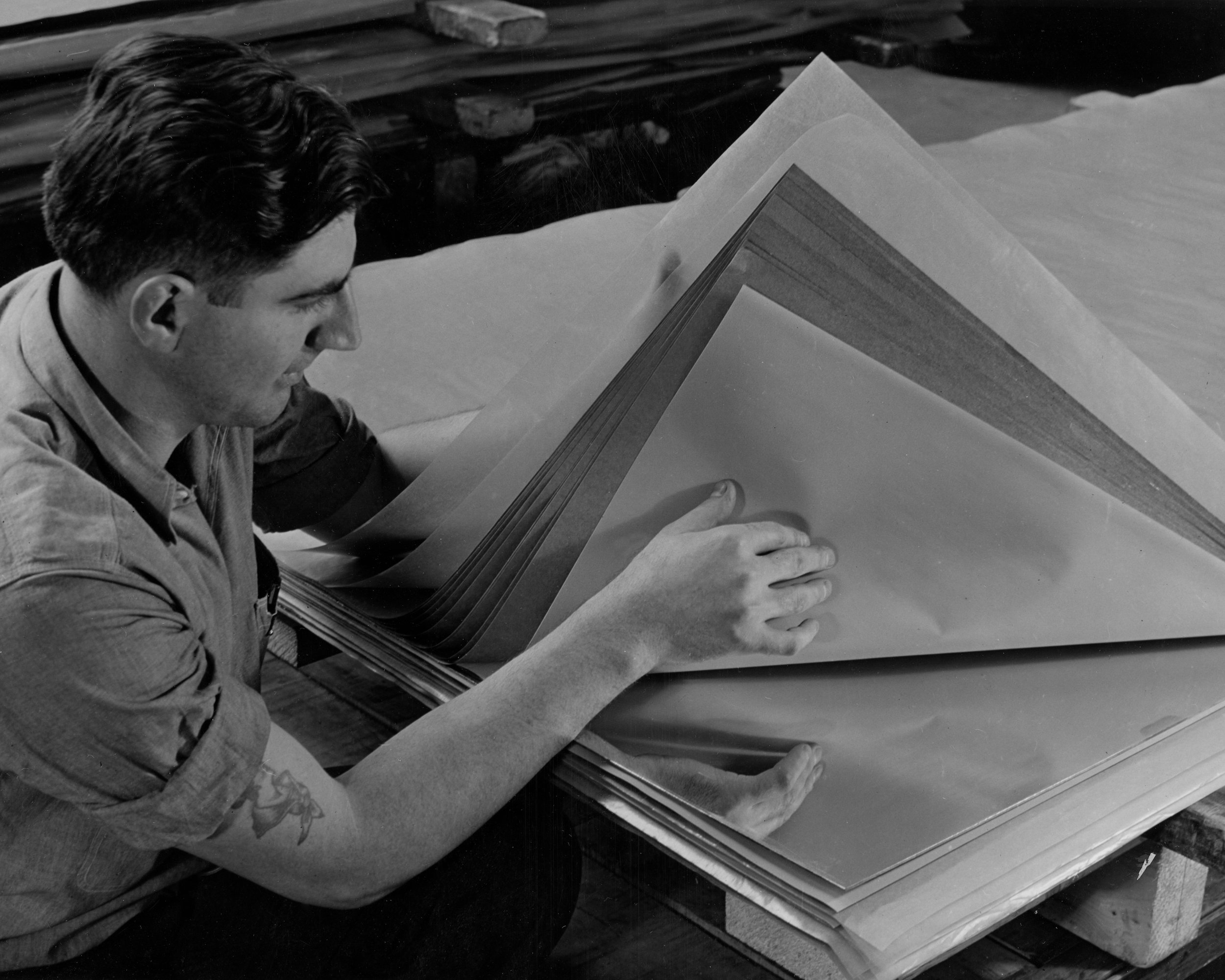 Heat and 150,000,000 pounds of pressure on these fourteen loose sheets of paper will produce a hard, white, waterproof plastic panel for the inside of a refrigerator. Next the polished steel plate at the bottom will go a sheet of white material resembling wall paper. On top of this will go a number of sheets of brown wrapping paper impregnated with synthetic resin, after which it will go to the moulding press. Westinghouse Micarta is also used for table tops, wall coverings and hundreds of other purposes.