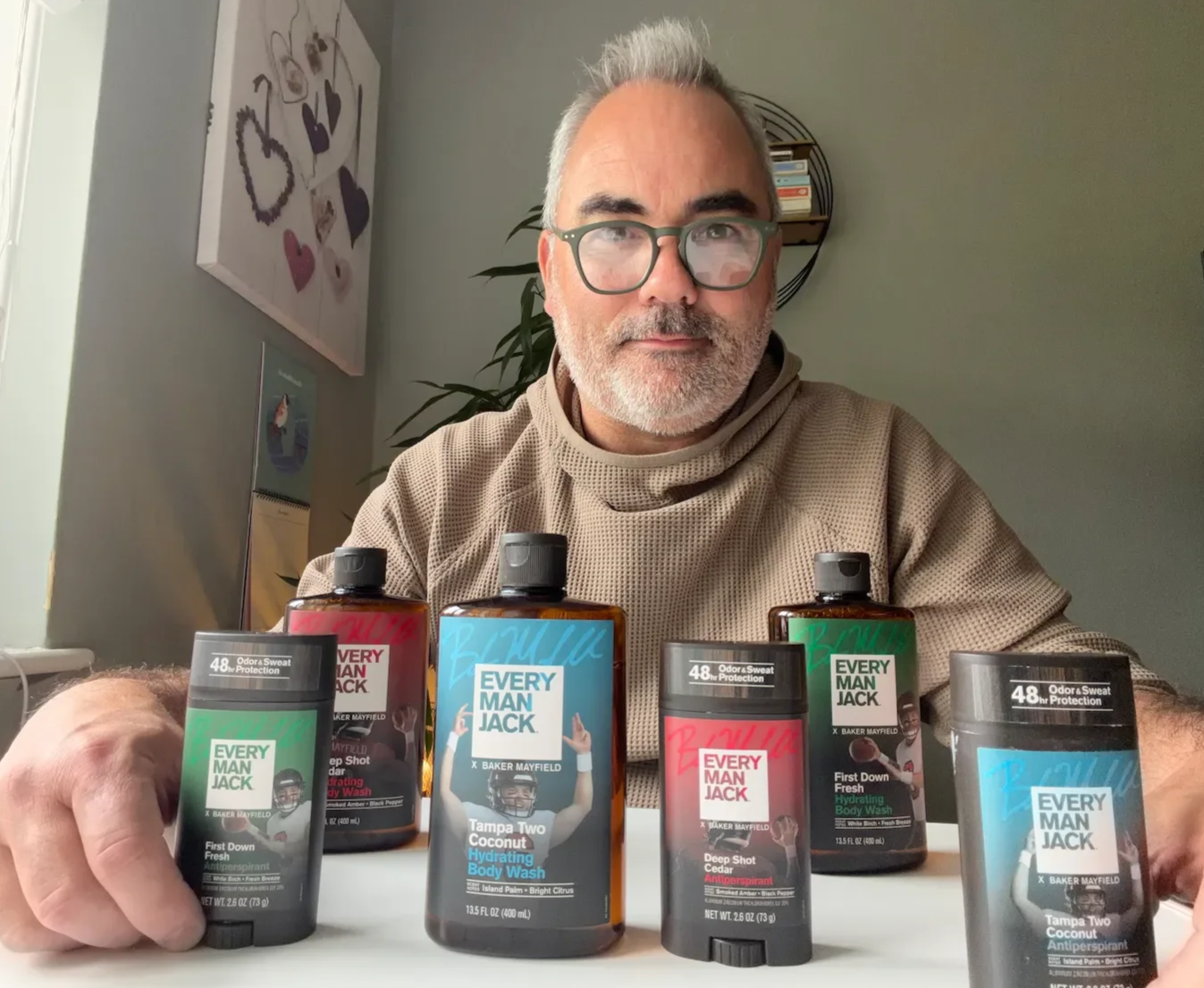Men's grooming reviewer seated behind the six Every Man Jack x Baker Mayfield body washes and antiperspirants during a hands-on product review.