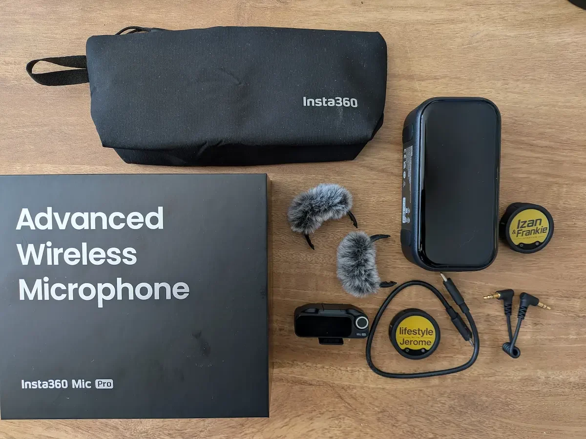 Insta360 Mic Pro full kit with box, carrying pouch, receiver, transmitter, windshields, cable and personalised E-Ink displays laid out on a wooden desk.