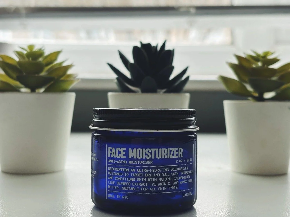 Blu Atlas Face Moisturizer jar on a desk in front of a window with potted plants in the background