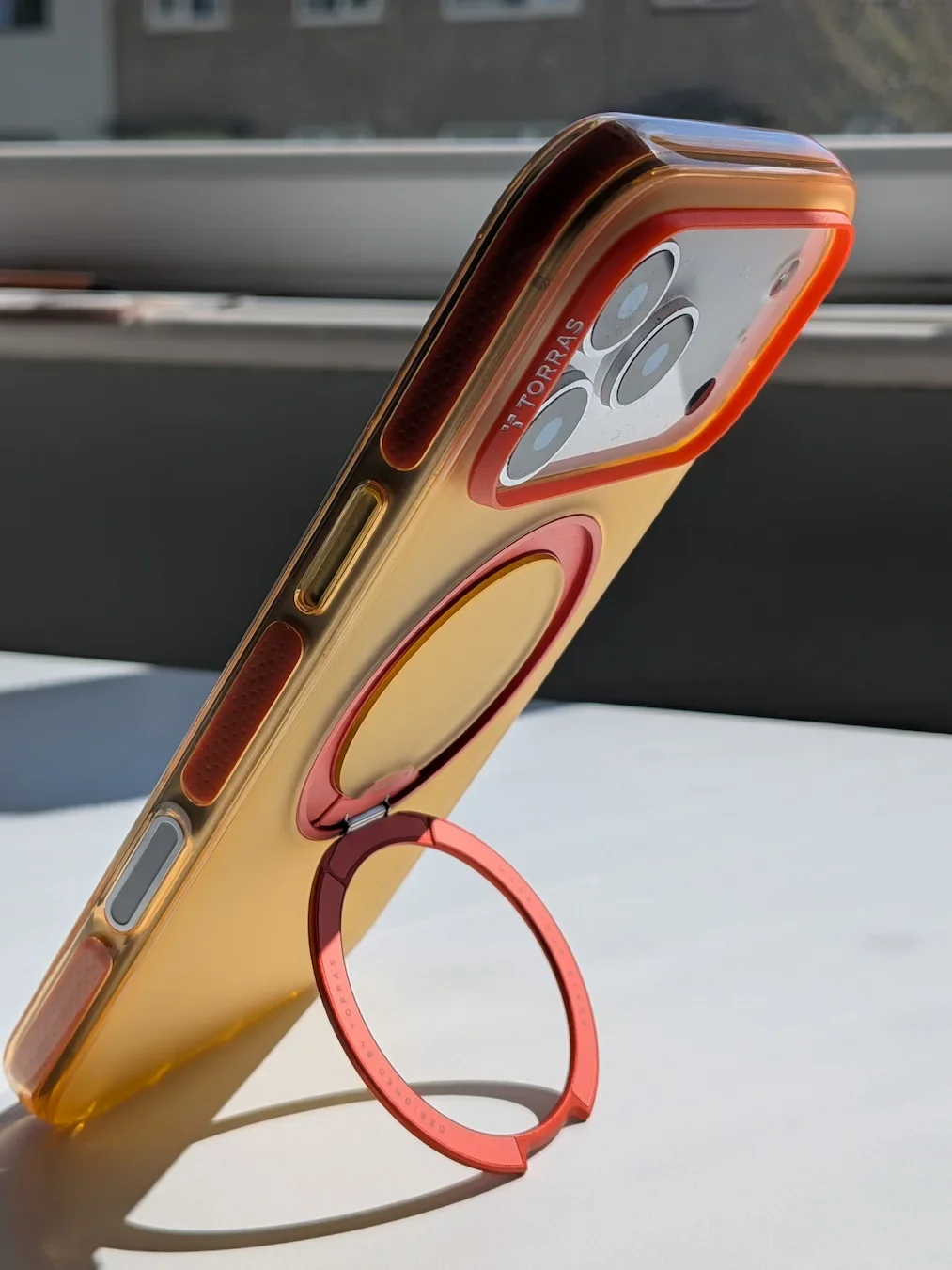 TORRAS Ostand Q3 Hue case in orange fitted on the iPhone 17 Pro Max with the ring stand open for hands-free viewing.