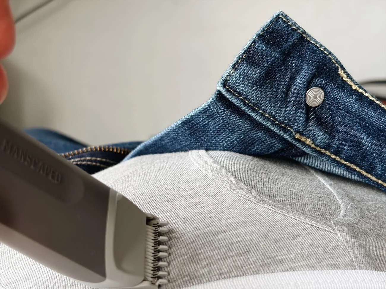 Close-up of the Manscaped Lawn Mower Go trimmer resting against a white T-shirt, with blue jeans visible in the background.