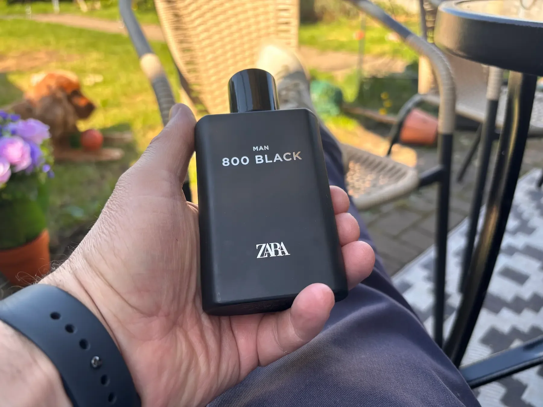 Jerome holding a bottle of Zara Man 800 Black cologne while sitting outside in his garden in Bristol