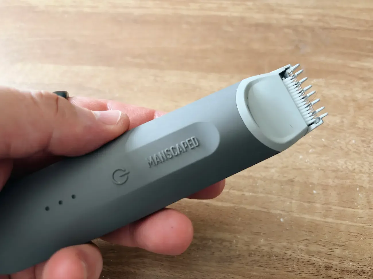 Close-up of the grey Manscaped Lawn Mower Go held in one hand, showing the attached trimming comb and rubberised grip.