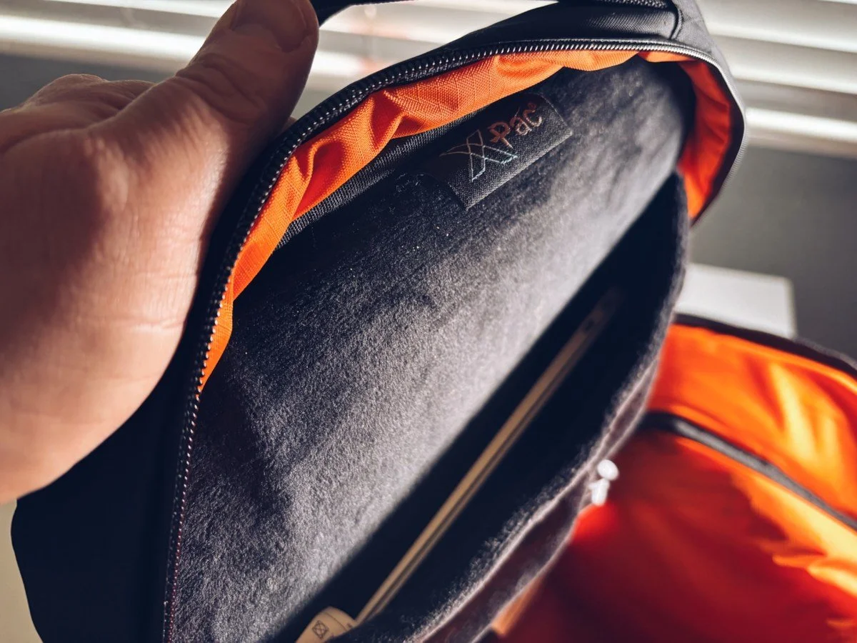 Close-up of the ADD1D D2D Essential Backpack laptop sleeve with soft lining, X-Pac label and high-visibility orange interior.
