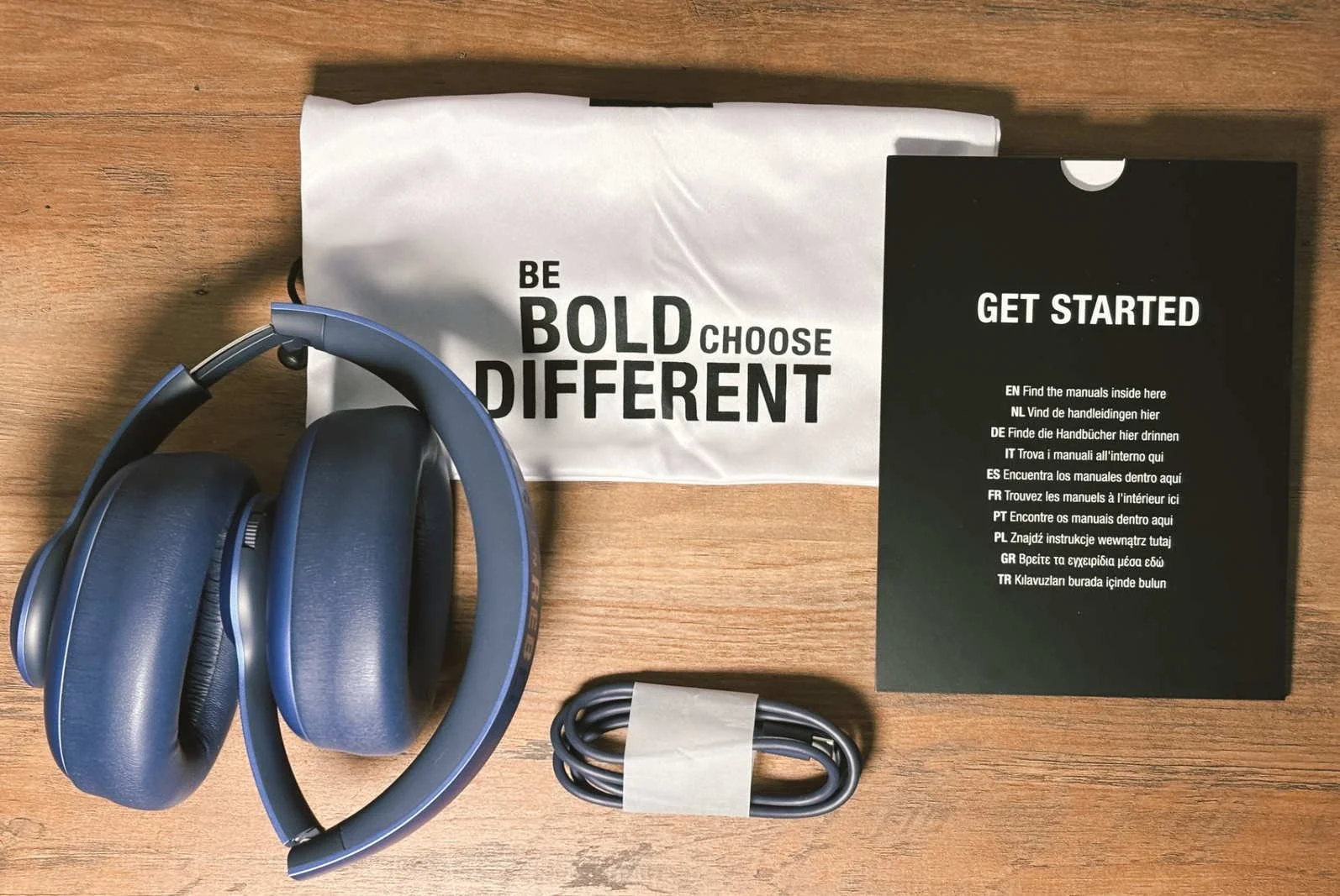 Fresh ’n Rebel Clam Ace 2 headphones with pouch, USB-C cable and ‘Get Started’ booklet laid out on a wooden table.