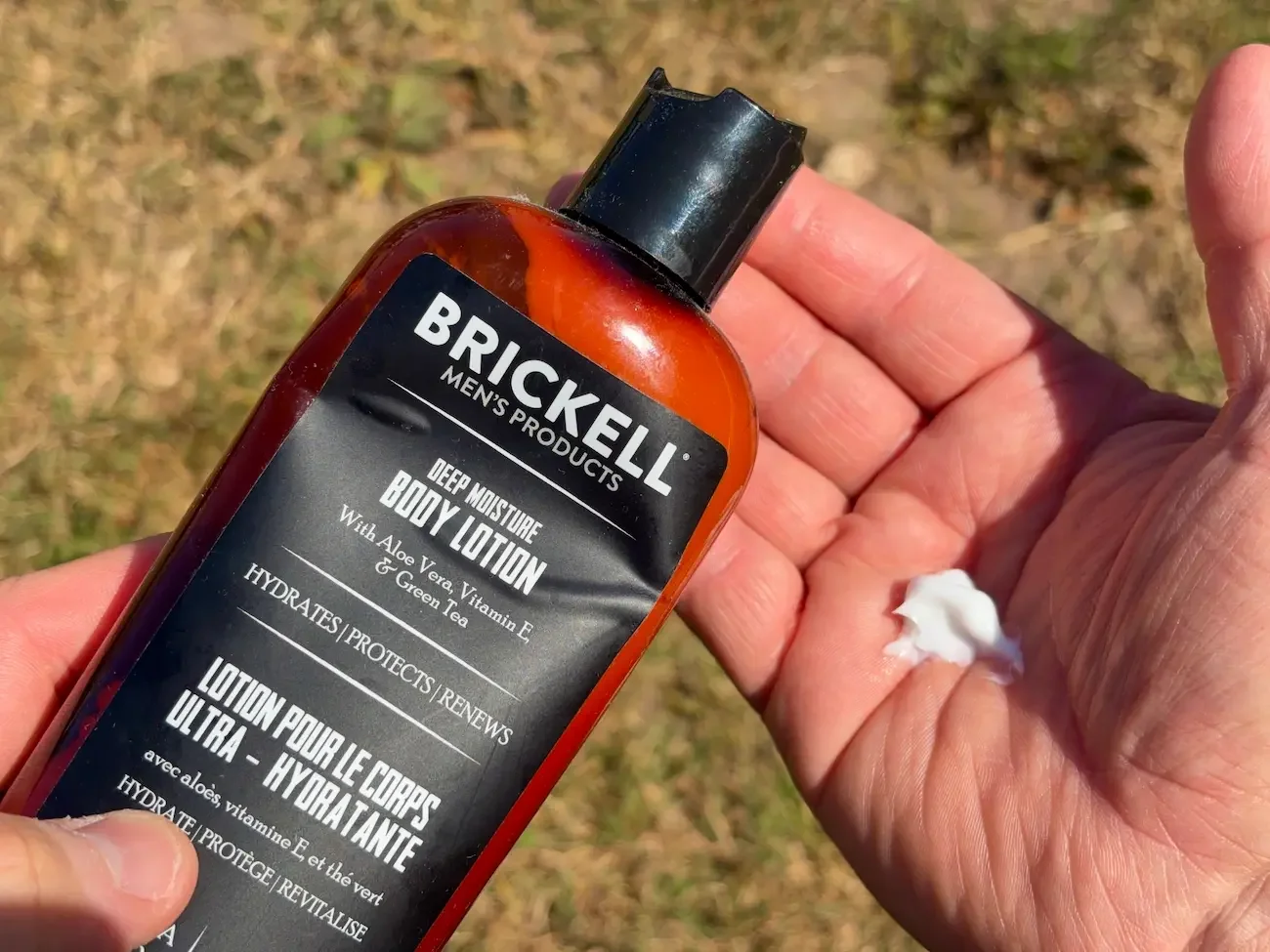Brickell Deep Moisture Body Lotion held outdoors with a small amount of lotion dispensed onto a hand.