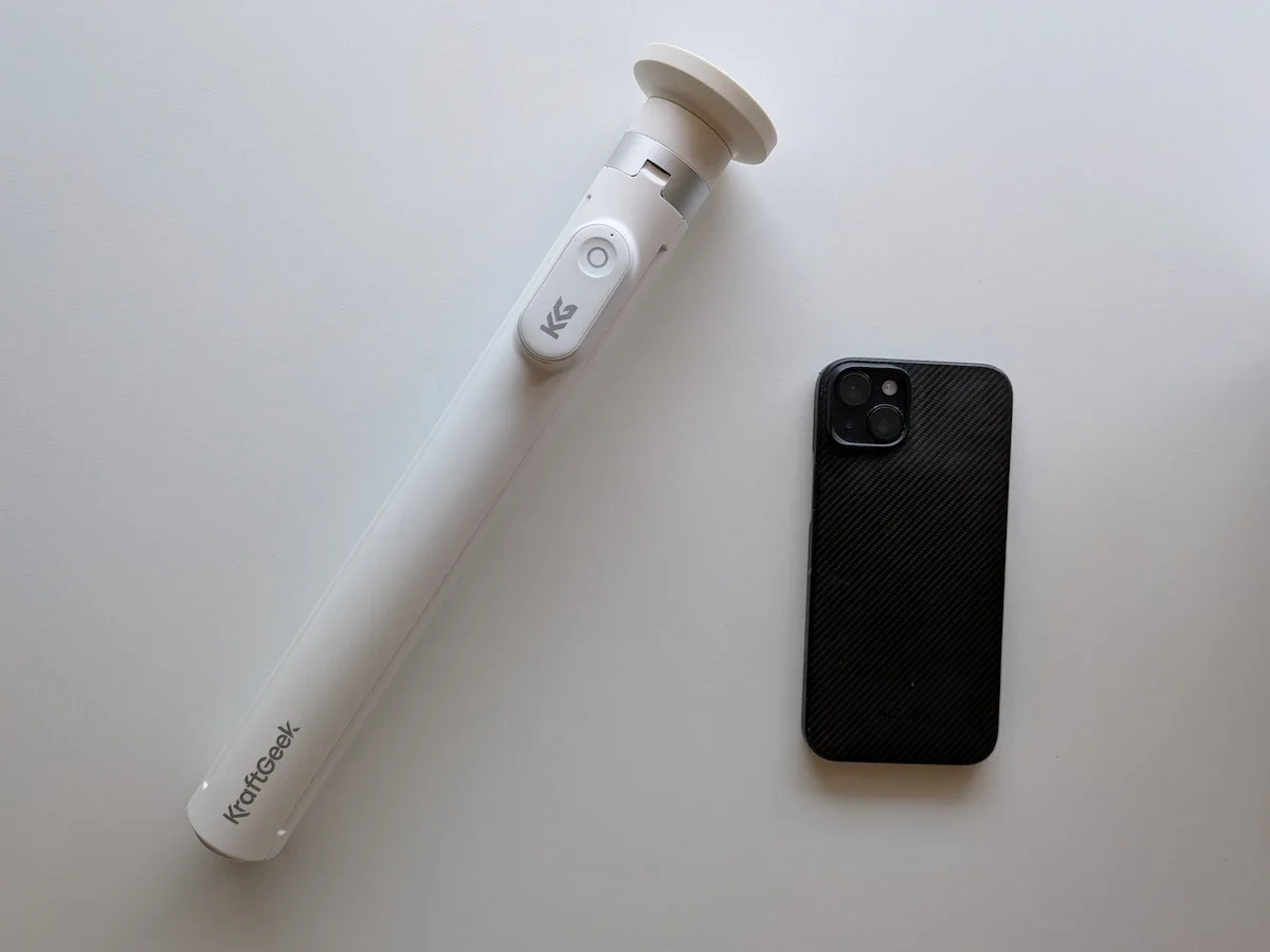 KraftGeek JustTap Magnetic Phone Tripod pictured beside an iPhone 15 Plus on a white background.