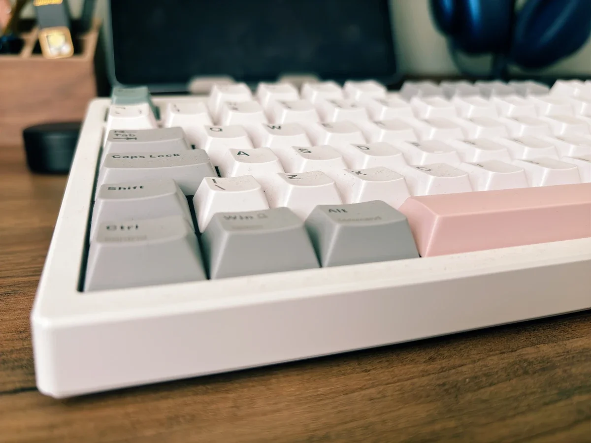 Close-up of the Epomaker TH87 mechanical keyboard showing the white, grey and pink keycaps on a wooden desk.