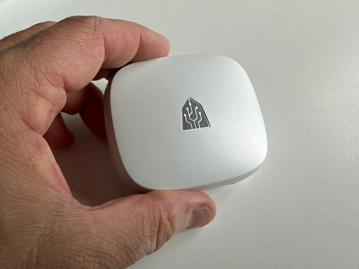 Close-up of the white Timekettle LiveTalk charging case held in one hand, showing the silver Timekettle logo