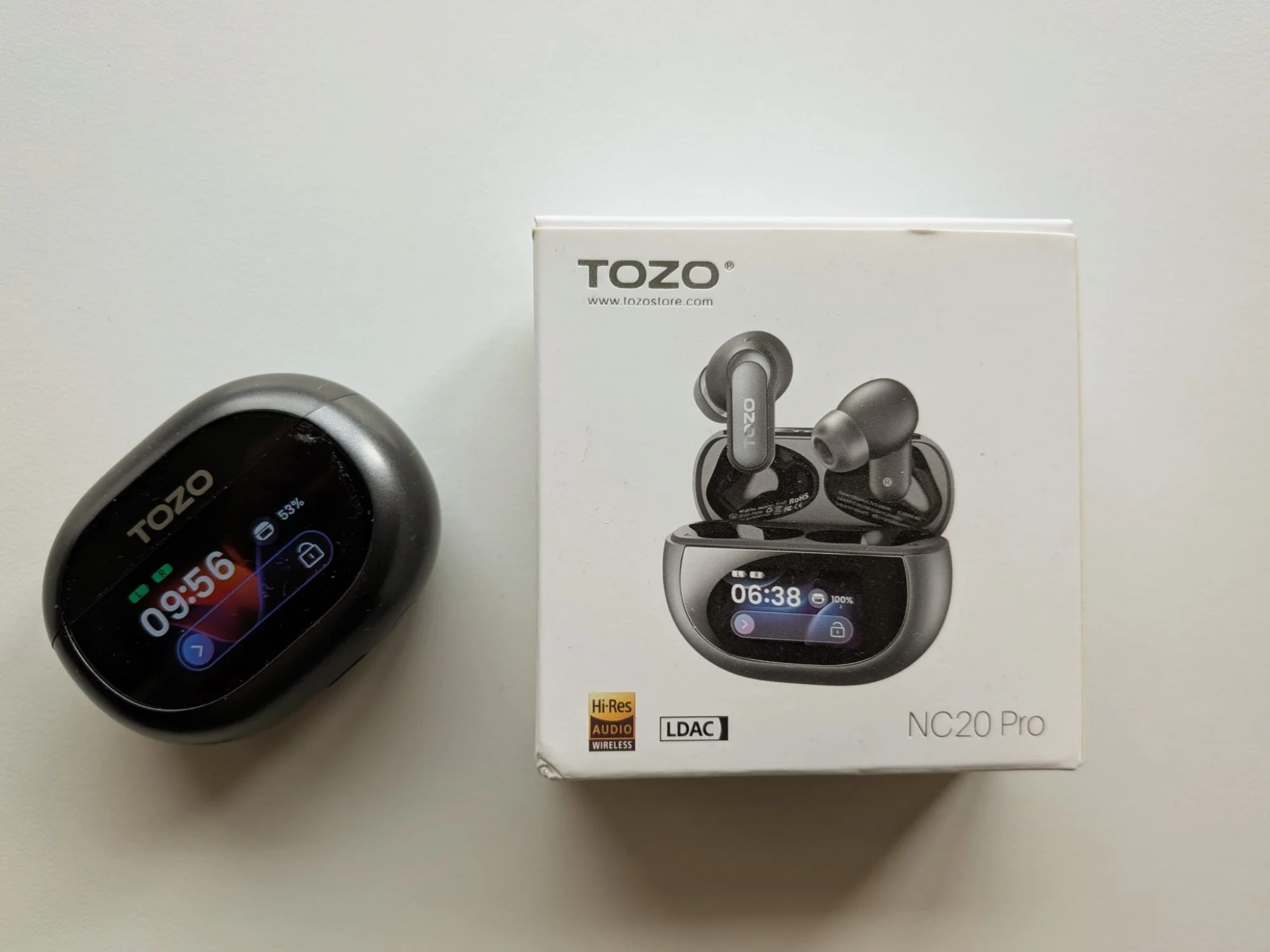 TOZO NC20 Pro earbuds with touchscreen charging case shown beside retail box, highlighting the smart display case and Hi-Res wireless audio branding.
