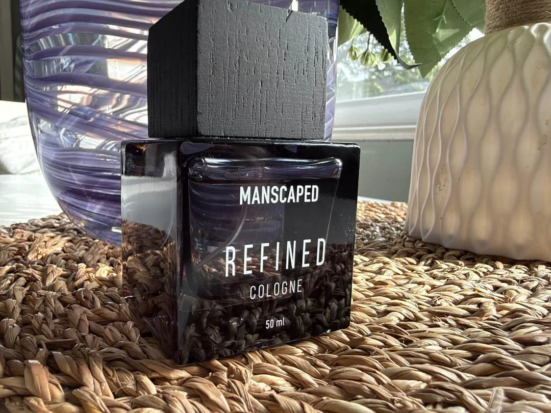 Close-up of the Manscaped Refined cologne bottle with its textured black cap on a woven placemat.