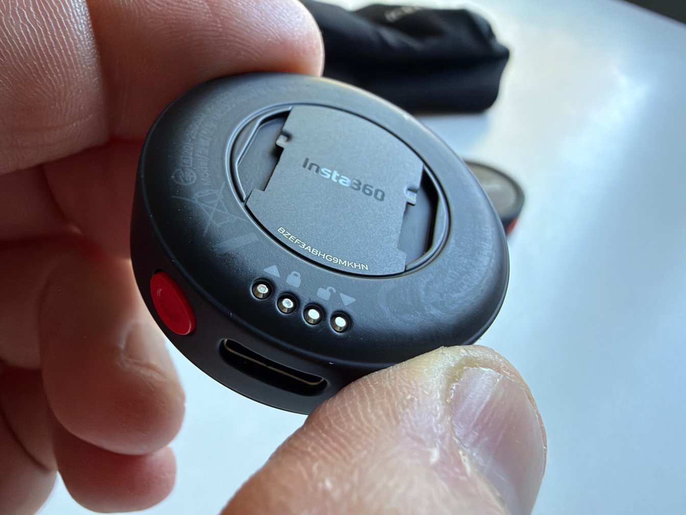 Rear view of a round Insta360 microphone transmitter showing the mounting system, contacts and side button.
