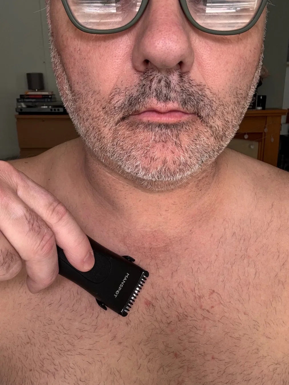 A close-up photograph of Jerome, the author of Dapper & Groomed, holding the black Manspot Body Groomer. He is guiding the trimmer over the stubble on his upper chest.