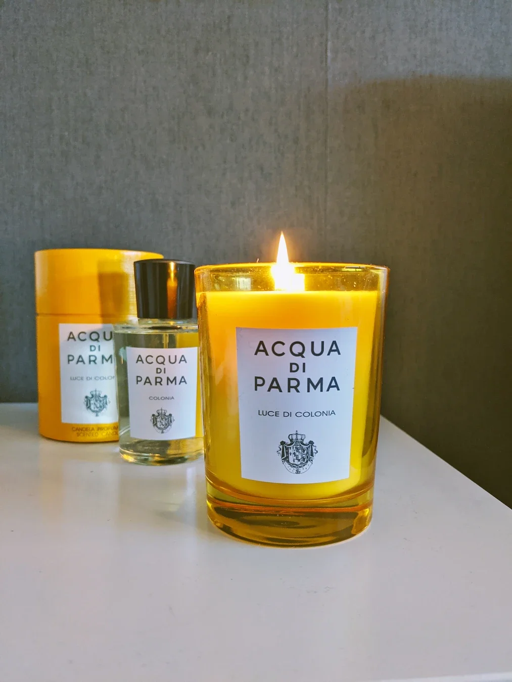 A bottle of Acqua di Parma Colonia cologne next to a lit Acqua di Parma 'Luce di Colonia' candle on a table