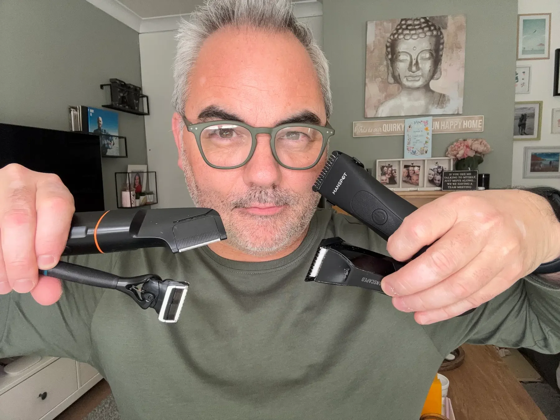 Jerome from Dapper & Groomed holding a selection of tested body hair trimmers, including Manscaped, Manspot, and a Gillette Intimate razor.