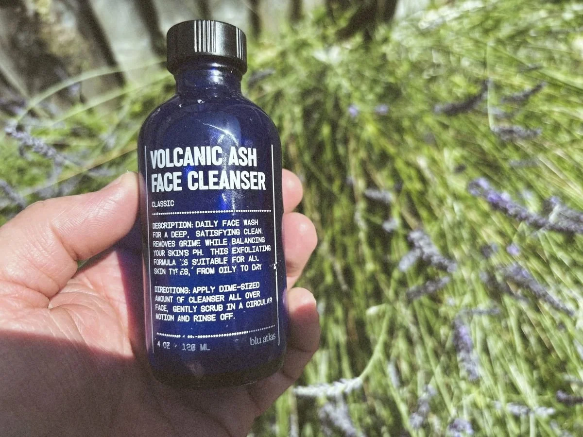 Blu Atlas Volcanic Ash Face Cleanser bottle held in hand outdoors with greenery background