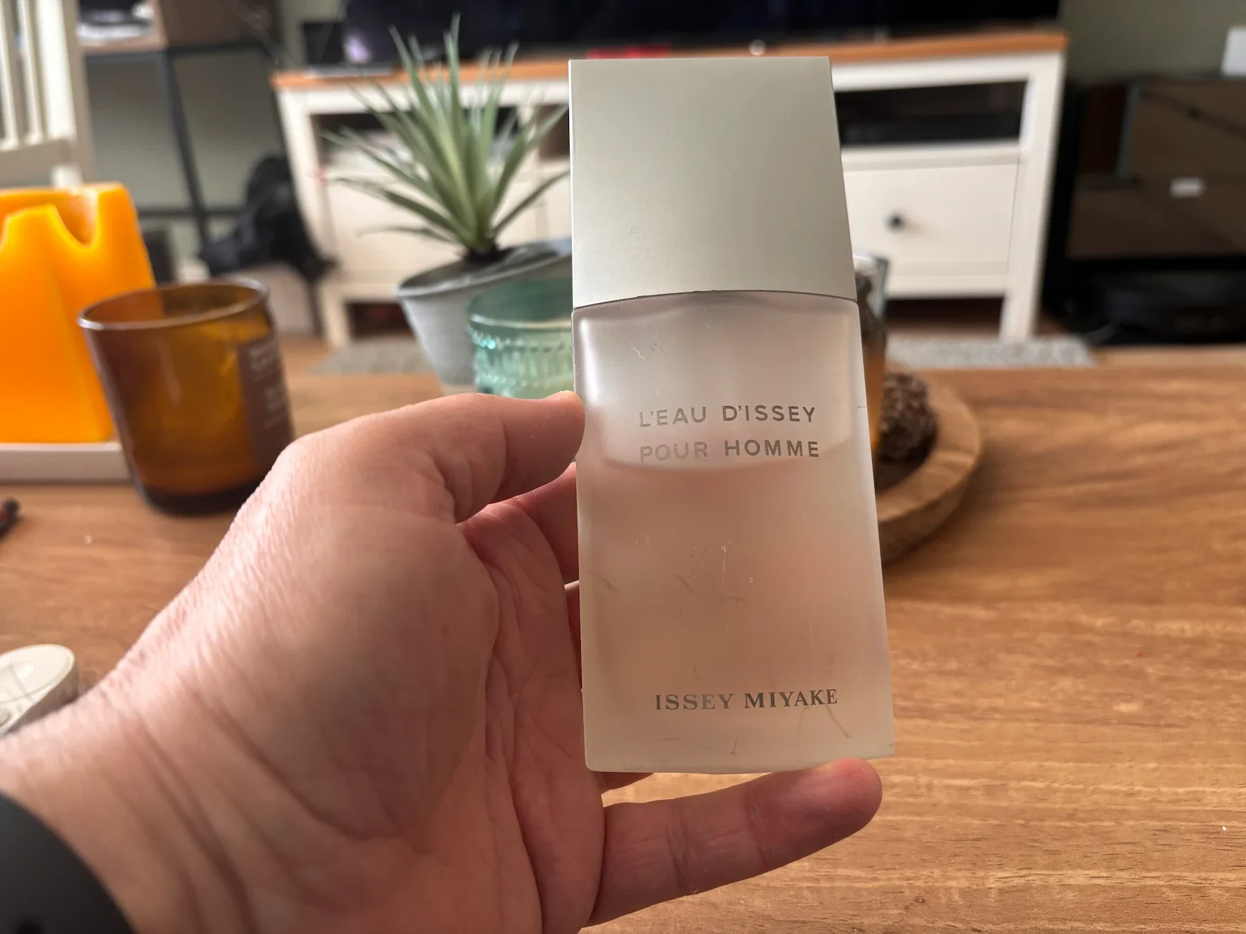 A bottle of L'Eau d'Issey Pour Homme by Issey Miyake on a wooden coffee table in a lived-in living room